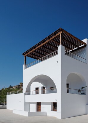 A modern white building with a wooden pergola on the upper floor, large arched windows, and a balcony with a railing. - Galma Luxury Homes (Kalymnos)