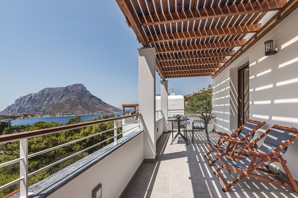 A balcony with a wooden pergola, a table with chairs, and a view of a mountain and sea. - Galma Luxury Homes (Kalymnos)