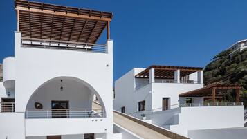 Un edificio moderno blanco con una pérgola de madera en el piso superior, una escalera que conduce al nivel superior y vistas a una colina.