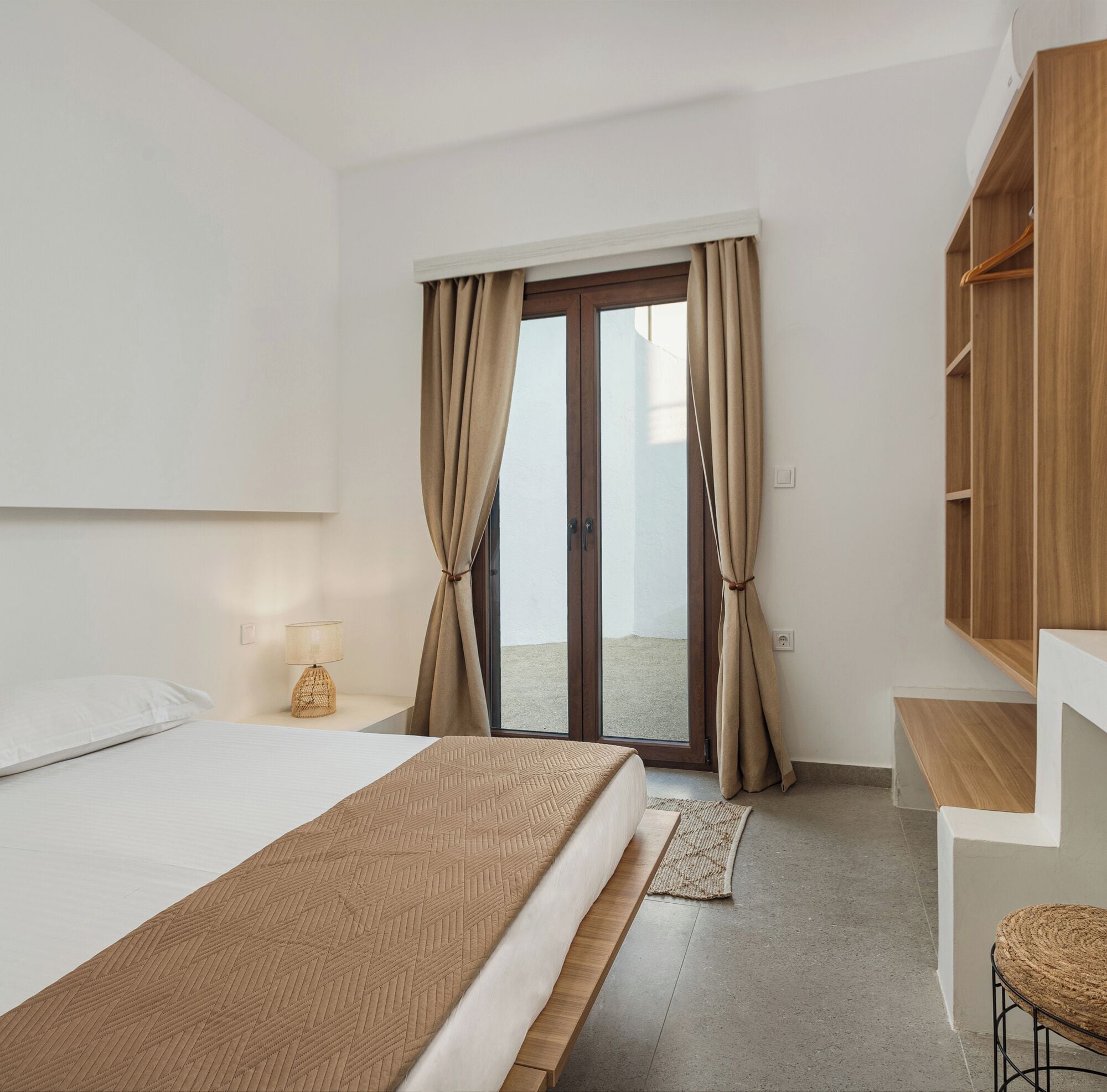 A hotel room with a bed, a desk, a wardrobe, and a view through a glass door.