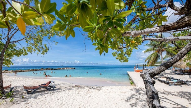 A beach with clear turquoise water, a sandy shore, and a few lounge chairs. - Spacious Villa Near Beach (Jan Thiel)