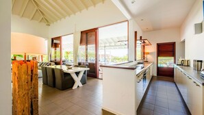 A modern kitchen with a central island, a dining area with a sofa, and large windows providing natural light. - Spacious Villa Near Beach (Jan Thiel)
