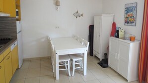 Cocina compacta con una mesa y sillas blancas, un armario amarillo, un refrigerador blanco y una lámpara colgante.