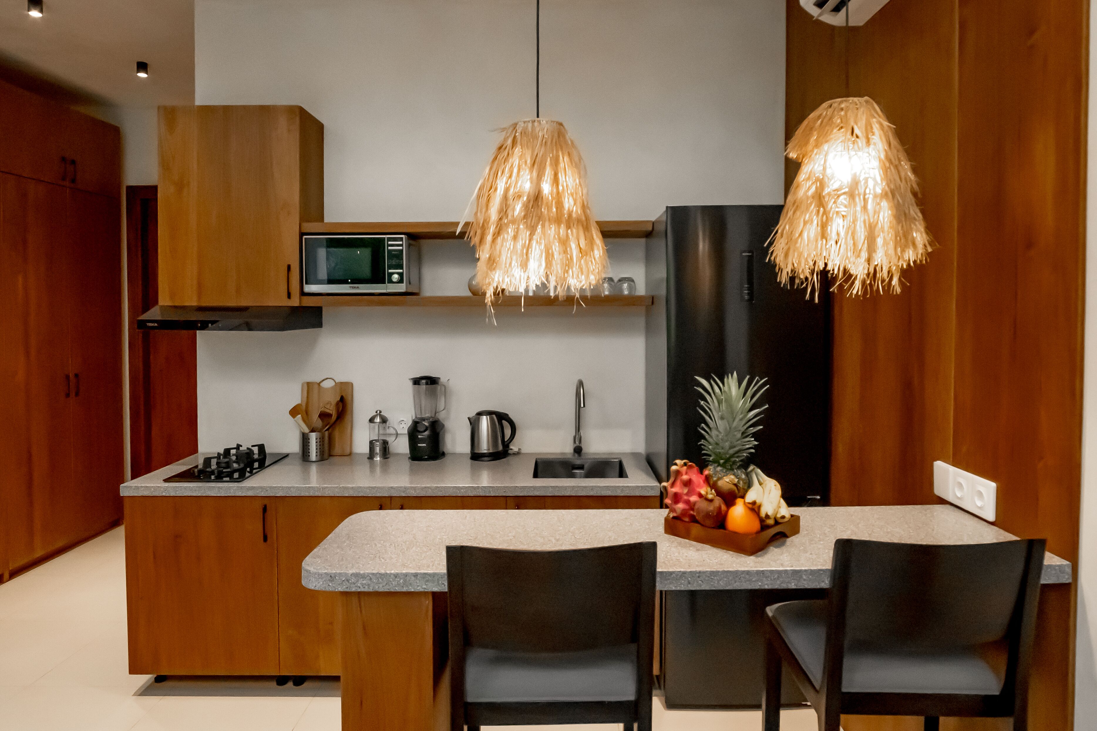 A modern kitchen with wooden cabinets, a built-in microwave, a black refrigerator, and a fruit bowl on the counter.
