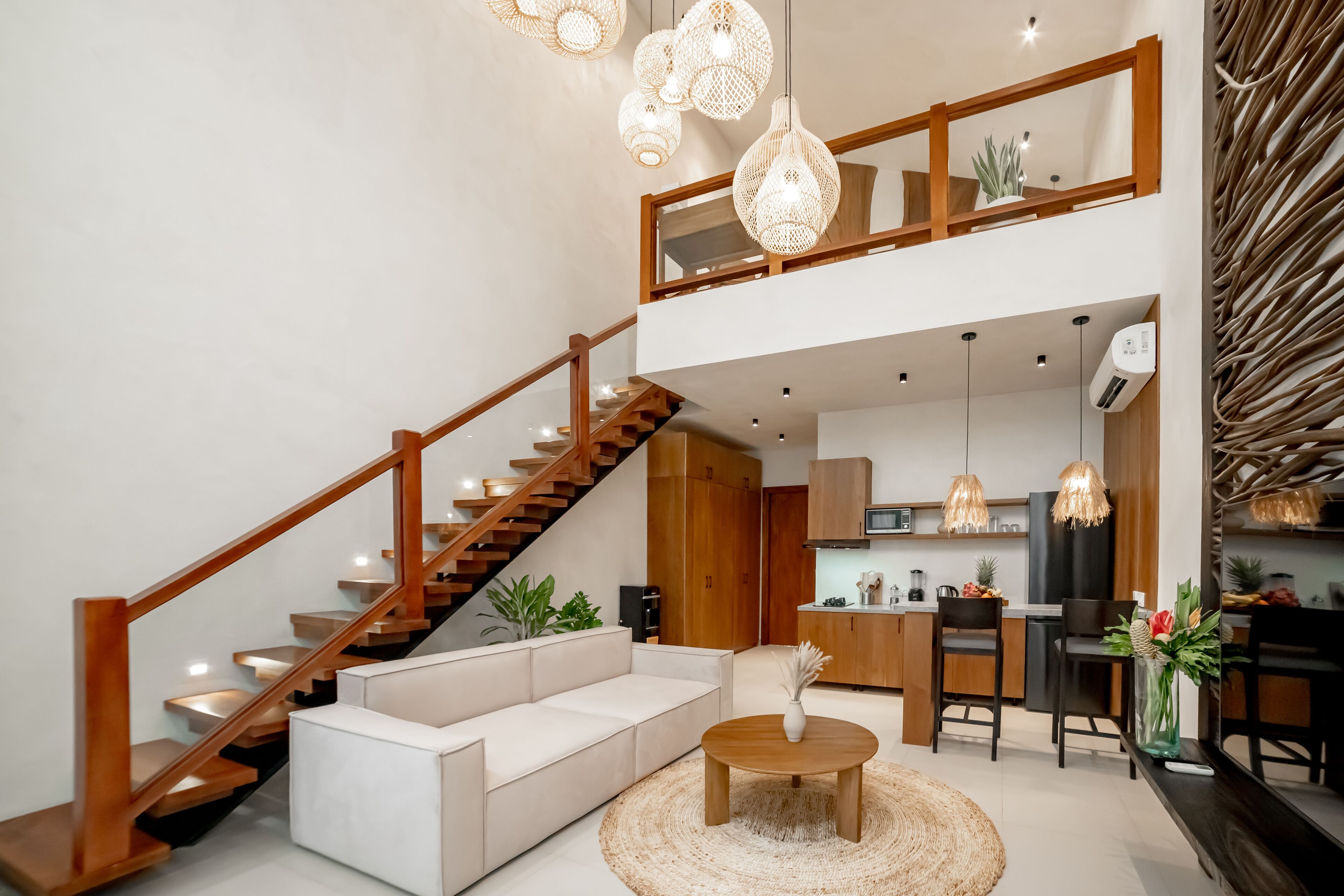 A modern living room with a staircase, a sofa, a coffee table, and a kitchen area in the background.