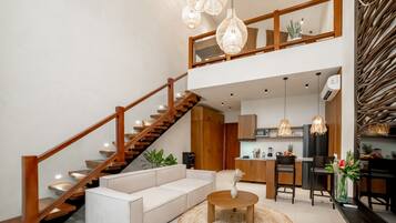 A modern living room with a staircase, a sofa, a coffee table, and a kitchen area in the background.