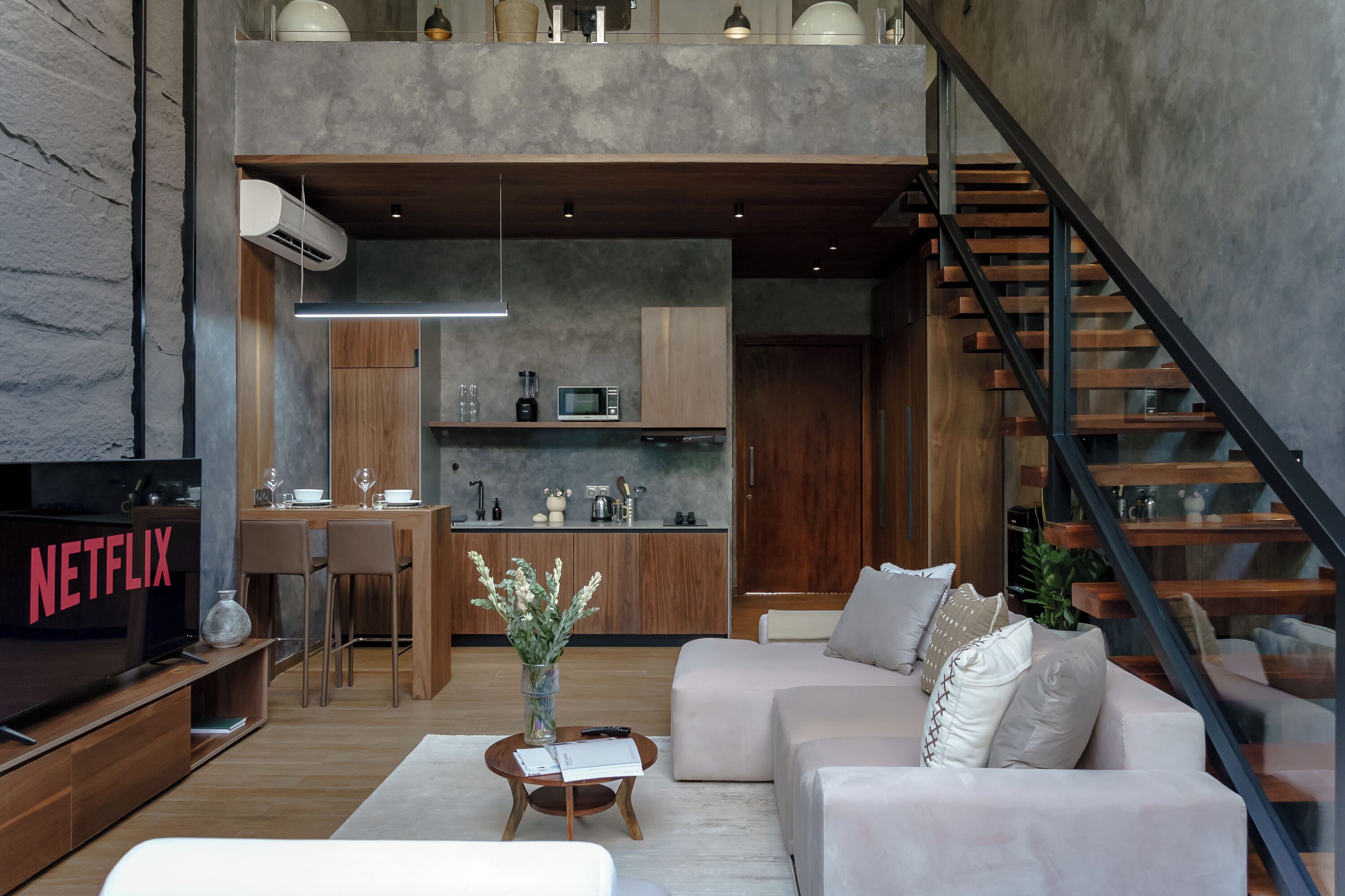 A modern living room with a flat-screen TV, a sofa, a coffee table, and a staircase.