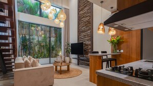A modern kitchen with a central island, a dining area with a round table, and a living room with a sofa and a TV. - Sunny Cuddles (Canggu)