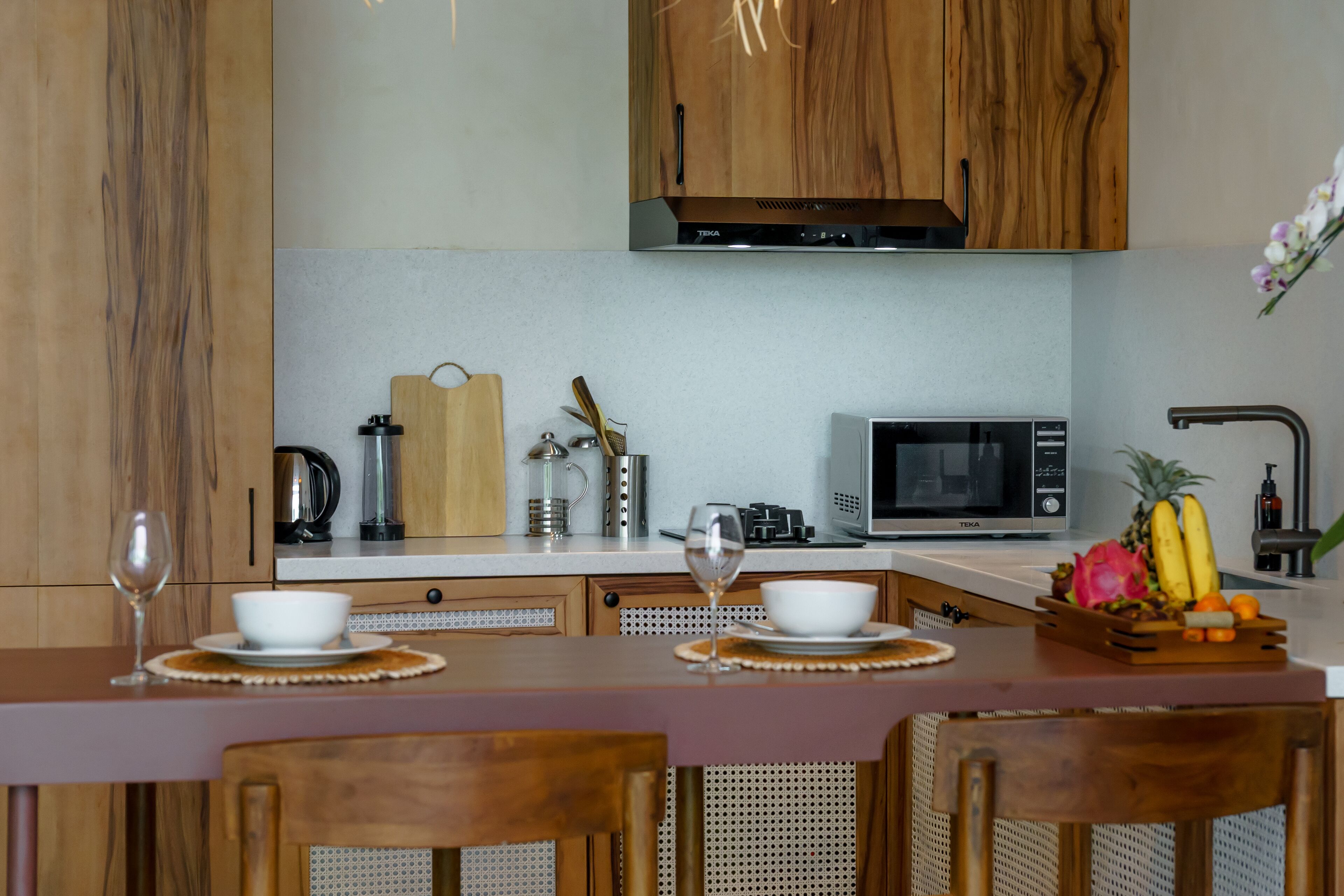 A modern kitchen with wooden cabinets, a microwave, and a fruit bowl on the counter.