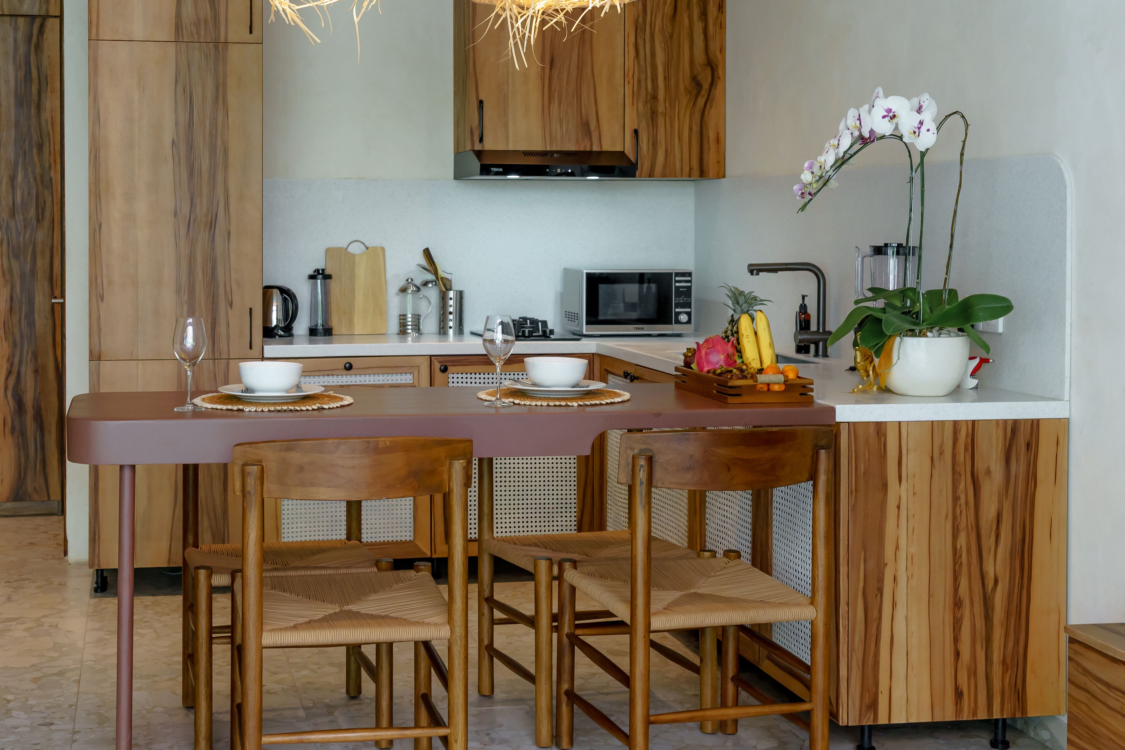 Una cocina moderna con armarios de madera, una isla central con sillas, un microondas y una orquídea en maceta.