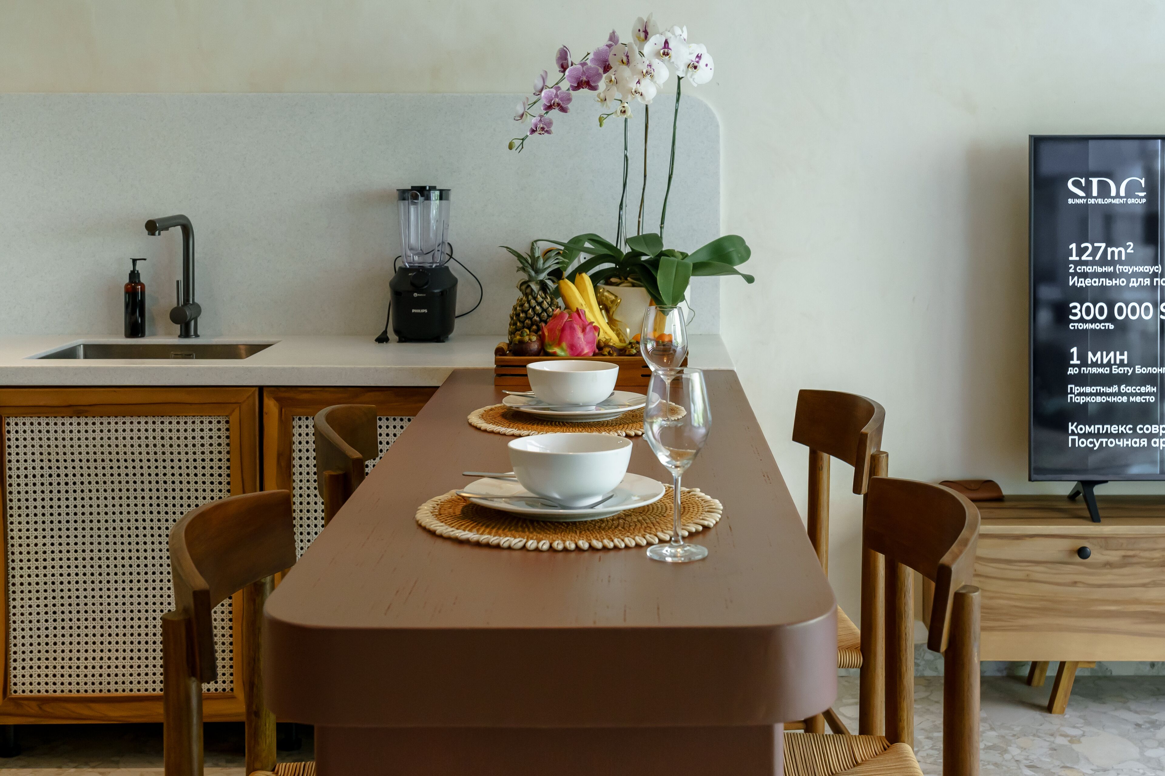 A modern kitchen with a wooden table set for dining, a blender, and a fruit bowl.