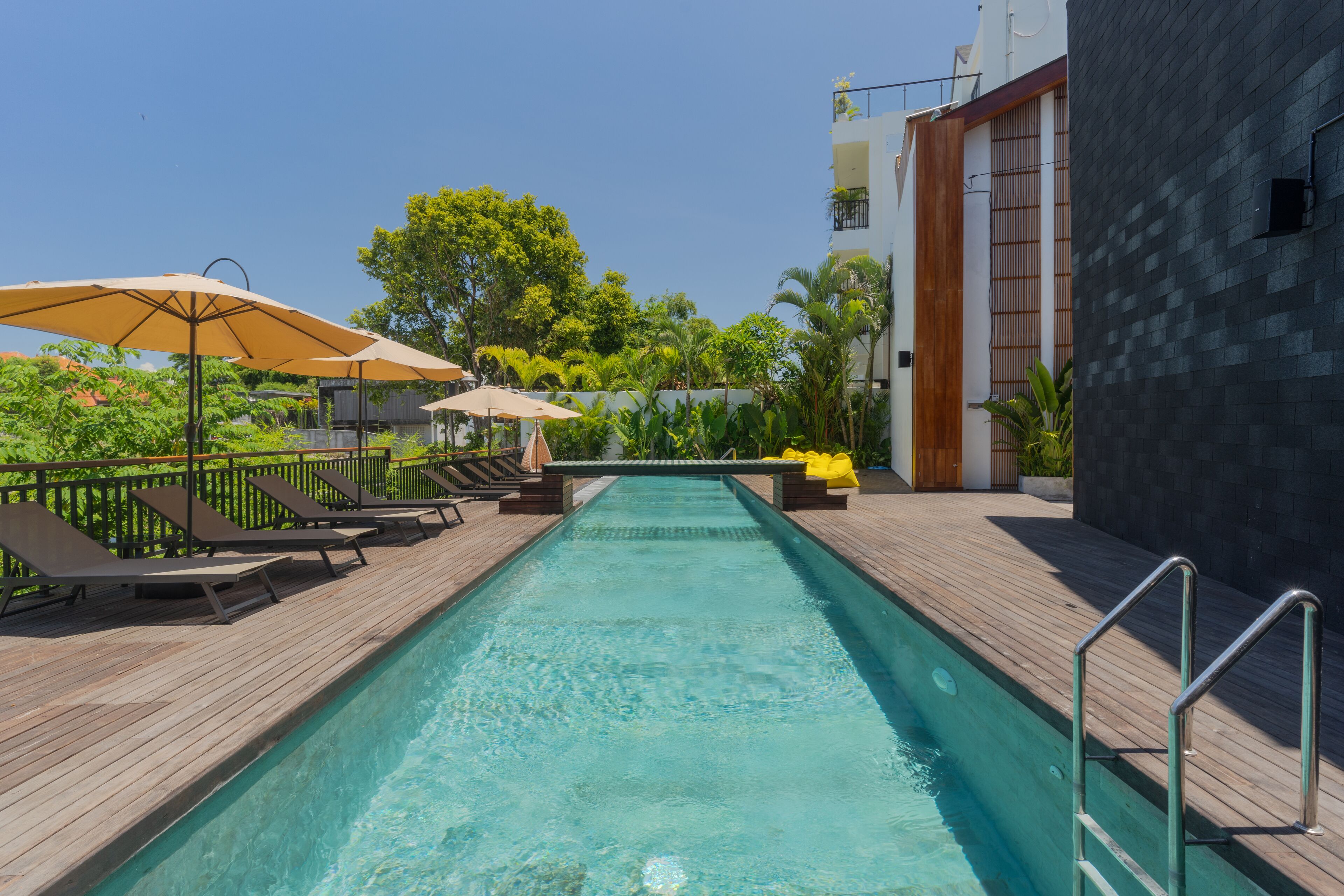 Ein Swimmingpool mit Liegestühlen und Sonnenschirmen, umgeben von Grünflächen und einem modernen Gebäude.