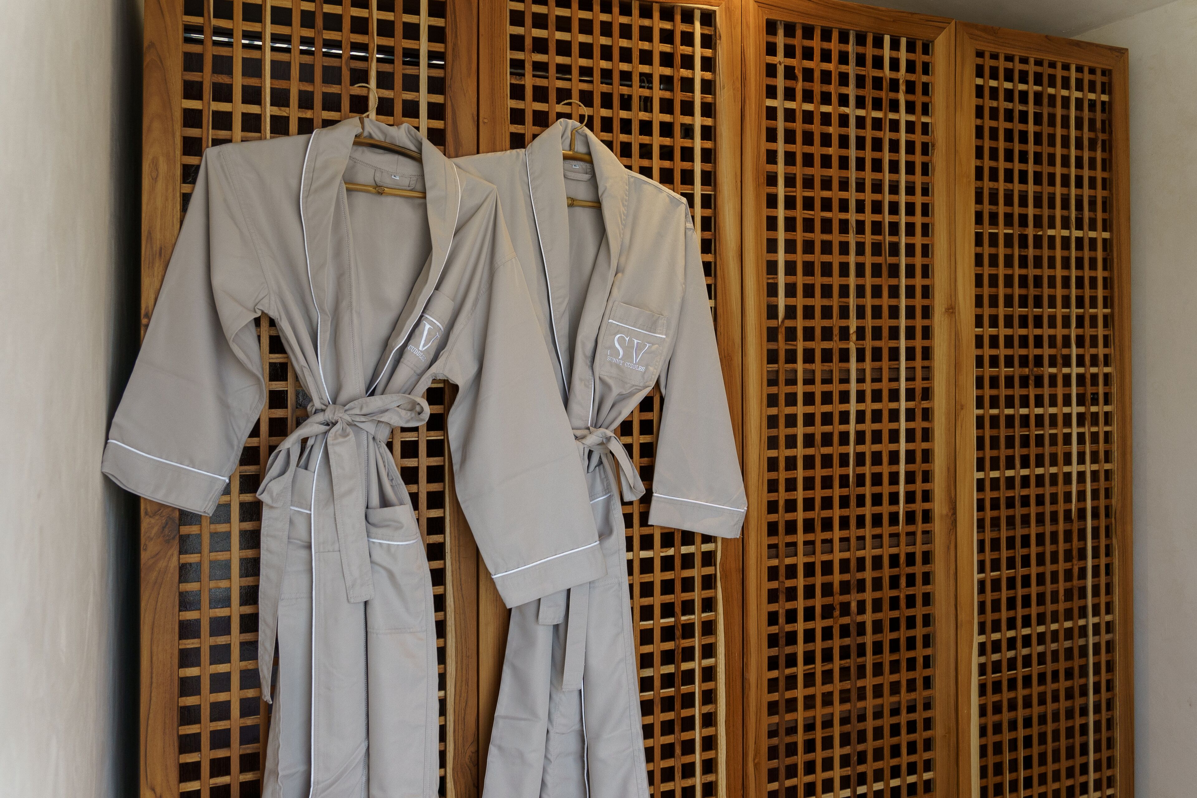Two grey robes tied at the waist, hanging on a wooden rack against a wooden lattice wall.