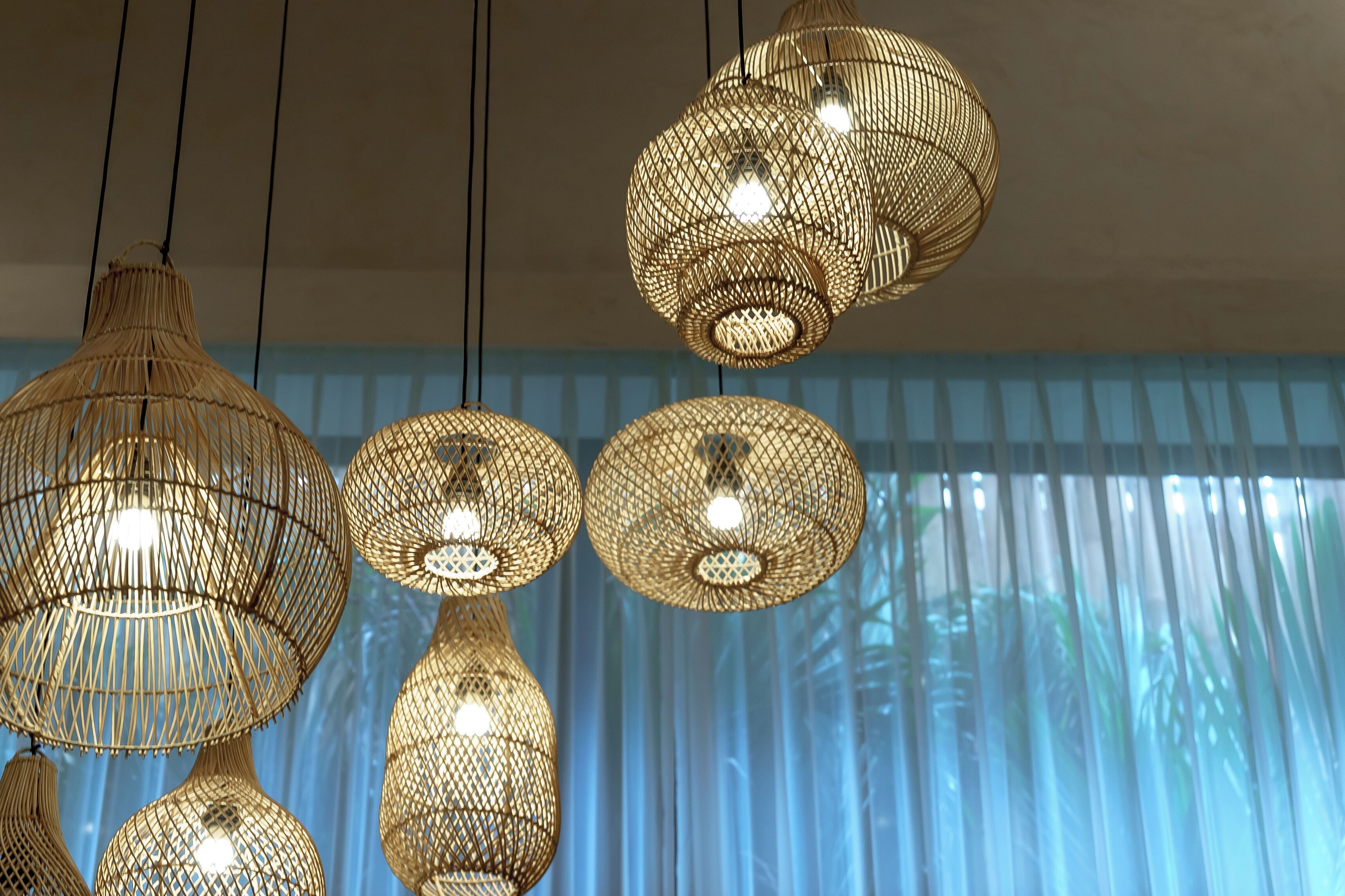 A room with hanging wicker lamps and a view of blue curtains.