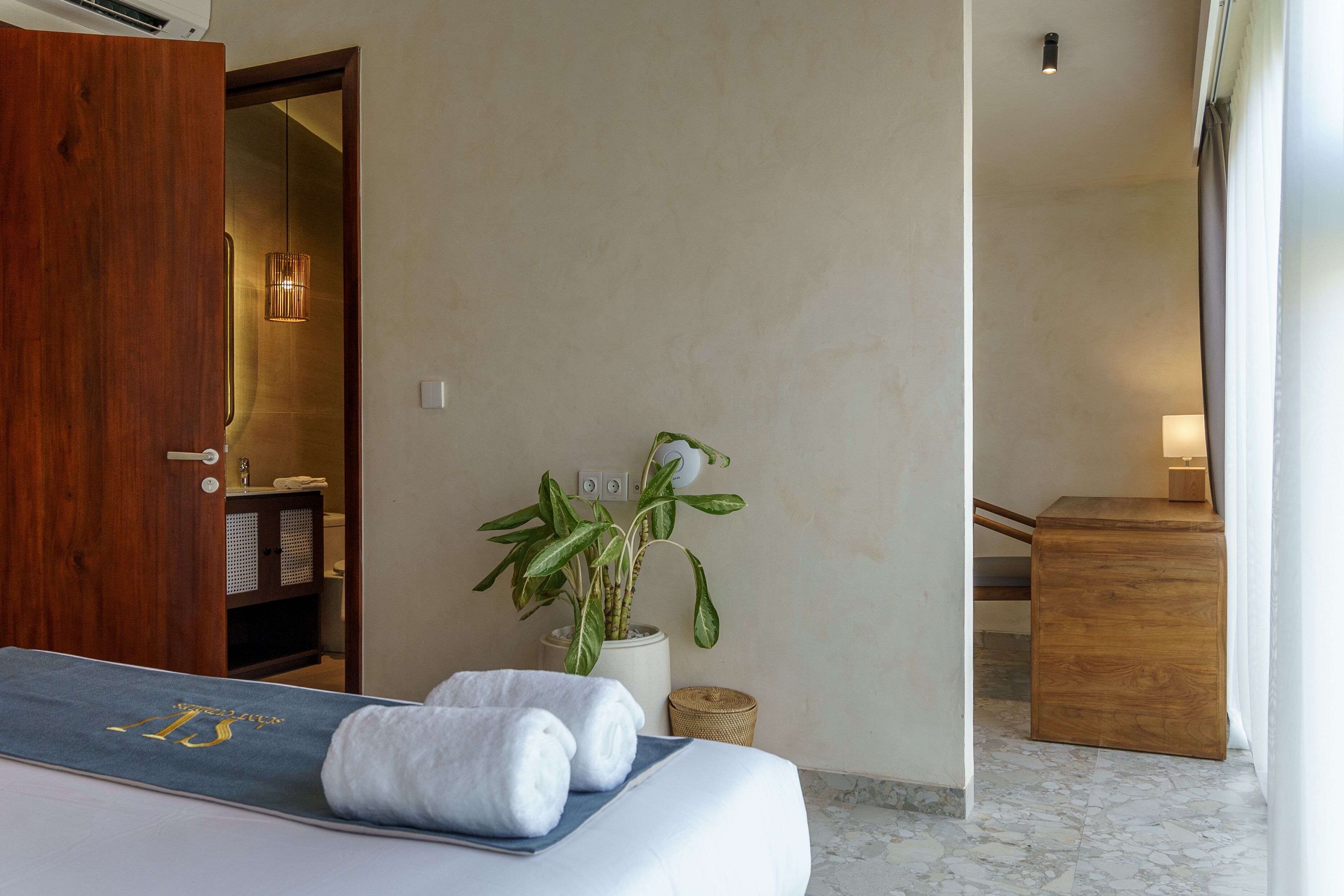 A hotel room with a bed, a wooden door, a plant, and a small wooden table.