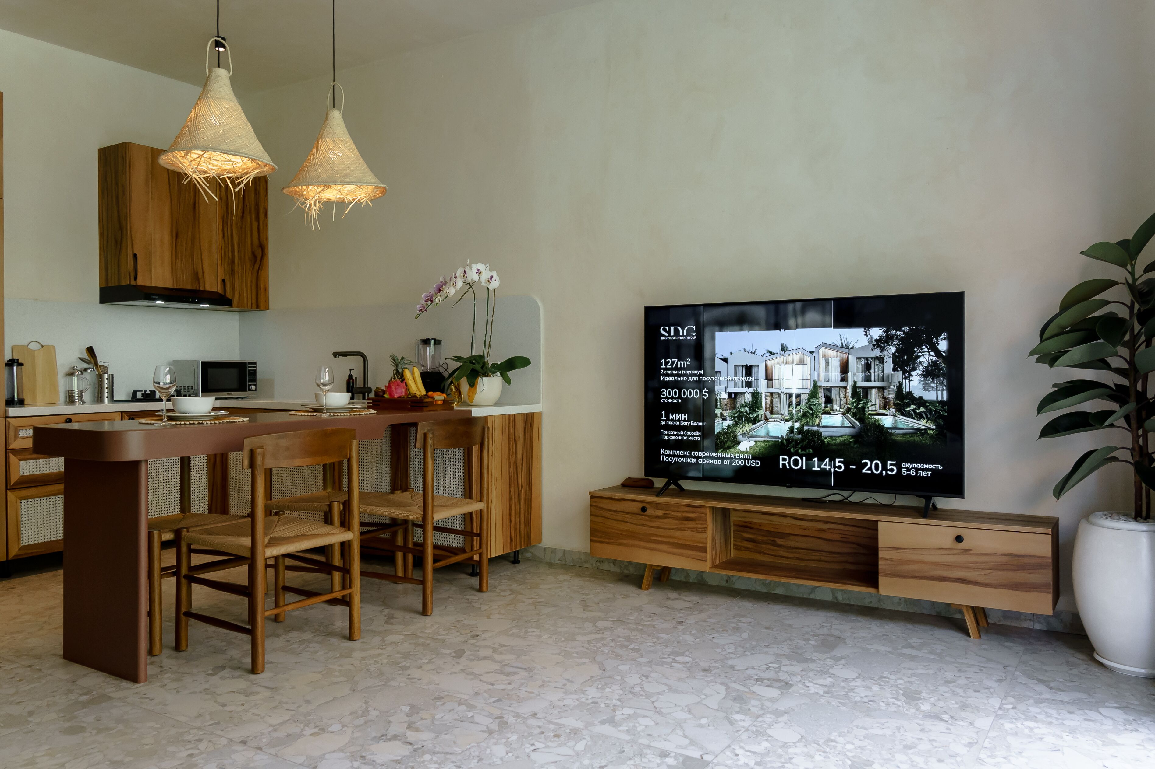 Een moderne keuken met een centraal eiland, houten kasten en een grote flatscreen televisie waarop informatie over vastgoed wordt getoond.