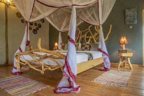A room with a bed featuring a wooden frame and a canopy. There are two bedside tables with lamps, a wall with decorative plates, and a wall with a framed quote. - Embogo Lodges  (Ishasha)