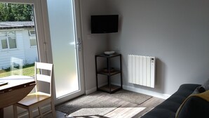 Ein modernes Wohnzimmer mit einer Couch, einem kleinen Holztisch, einem an der Wand montierten Fernseher und einer Essecke mit Stuhl und Tisch.