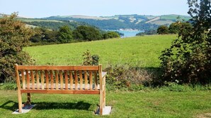 Eine hölzerne Bank in einem grünen Feld mit einem schönen Ausblick auf Hügel und ein Gewässer in der Ferne.