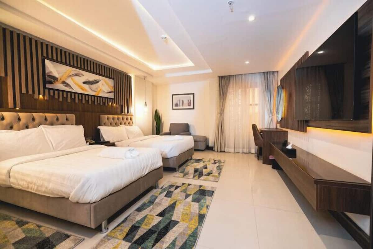 A modern hotel room with two beds, a desk, a TV, and a large window with curtains.