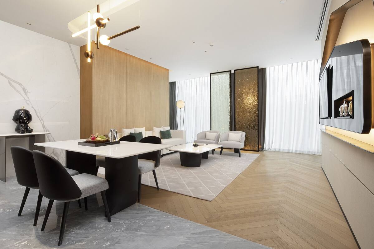 A modern living room with a dining area, featuring a large wooden panel wall, a white sofa, a coffee table, and a TV mounted on the wall.