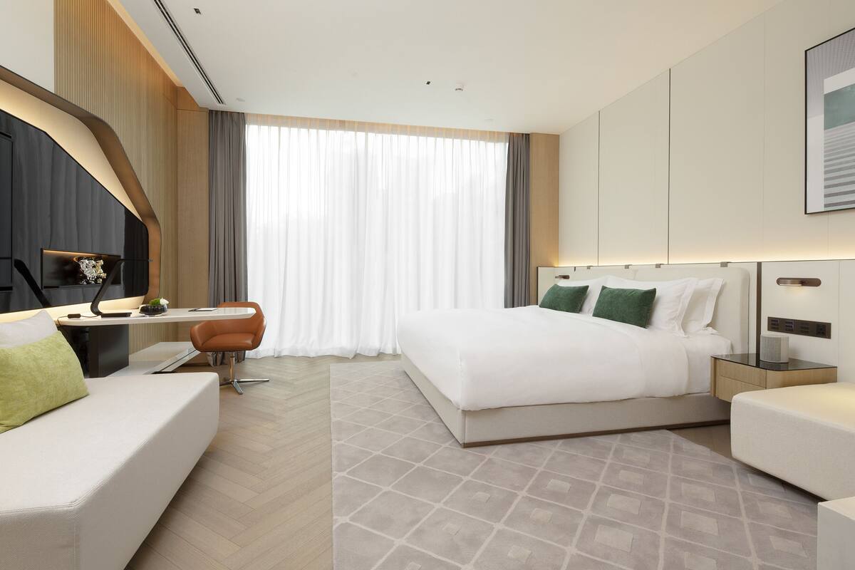 A modern hotel room with a large bed, a desk, a chair, and a sofa.