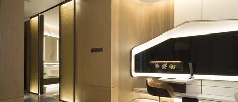 A modern hotel room with a wooden finish, a large flat-screen TV, a desk with a chair, and a separate bathroom area.
