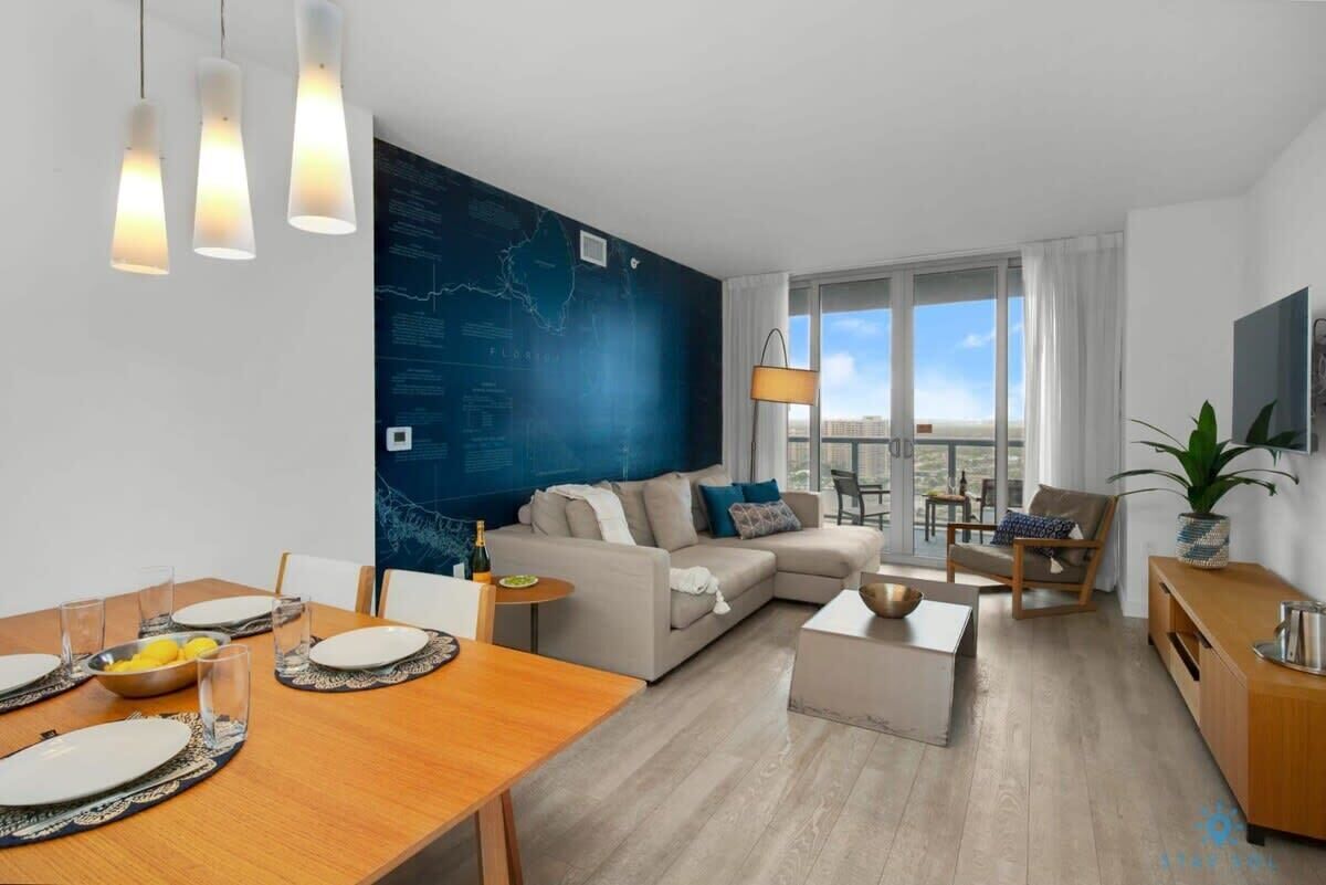 Ein modernes Wohnzimmer mit Sofa, Couchtisch und Essbereich. Ein großes Fenster bietet Blick auf die Stadt.