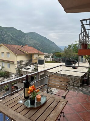 A terrace with a table set for two, a bottle of wine, and a candle. The terrace overlooks a mountainous landscape with buildings in the background. - Themis Apart Hotel (Kotor)