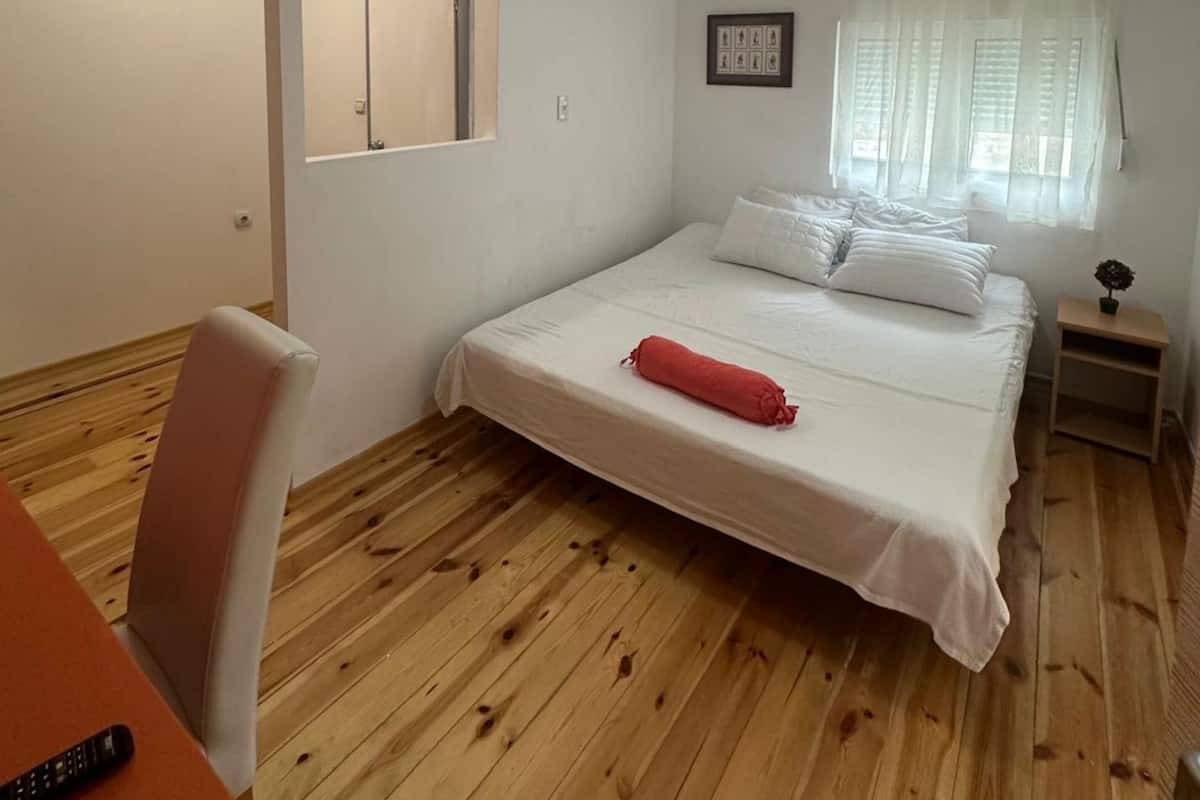 A small, clean room with a single bed, a chair, a table, and a window with curtains.