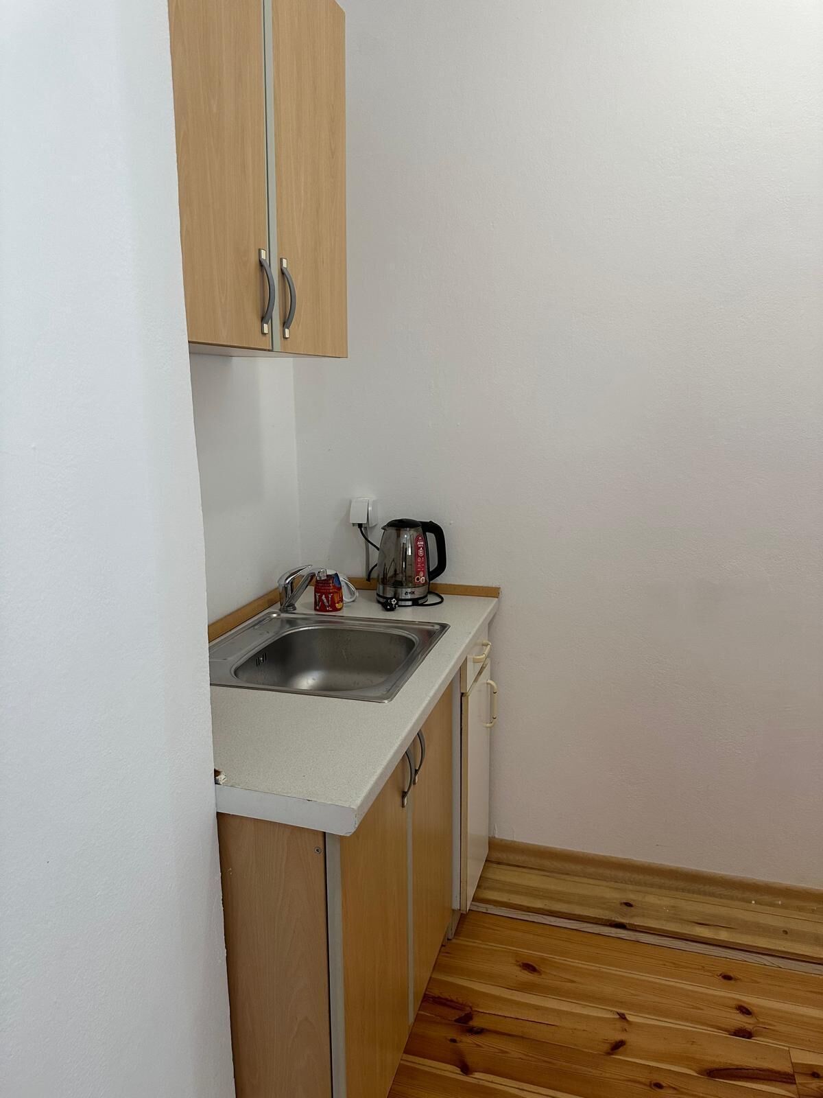 Una pequeña kitchenette con un lavamanos, una tetera y un armario.