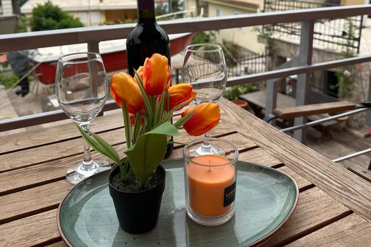 A table with a wine bottle, tulips, and a candle on a balcony overlooking a mountainous landscape.