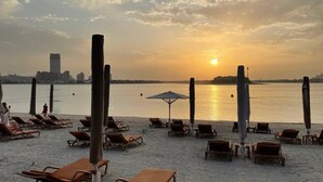 Ein Strand mit Liegestühlen und Sonnenschirmen, ruhigem Meer und einem Sonnenuntergang im Hintergrund.