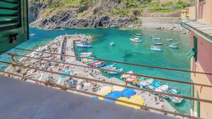 A coastal view from a balcony with boats docked at a pier, rocky cliffs, and a building with a balcony. - Maemuna Sea View Apartment (Vernazza)