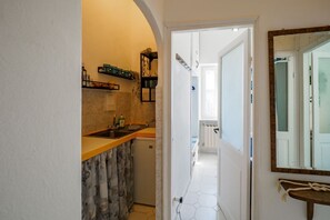 Un couloir étroit avec un coin cuisine, une porte donnant sur une autre pièce et un miroir accroché au mur.