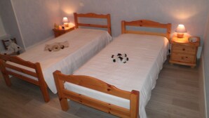 A small, simple room with two wooden beds, each with a nightstand and a lamp. - Gite a la Campagne (La Roche-Vanneau)