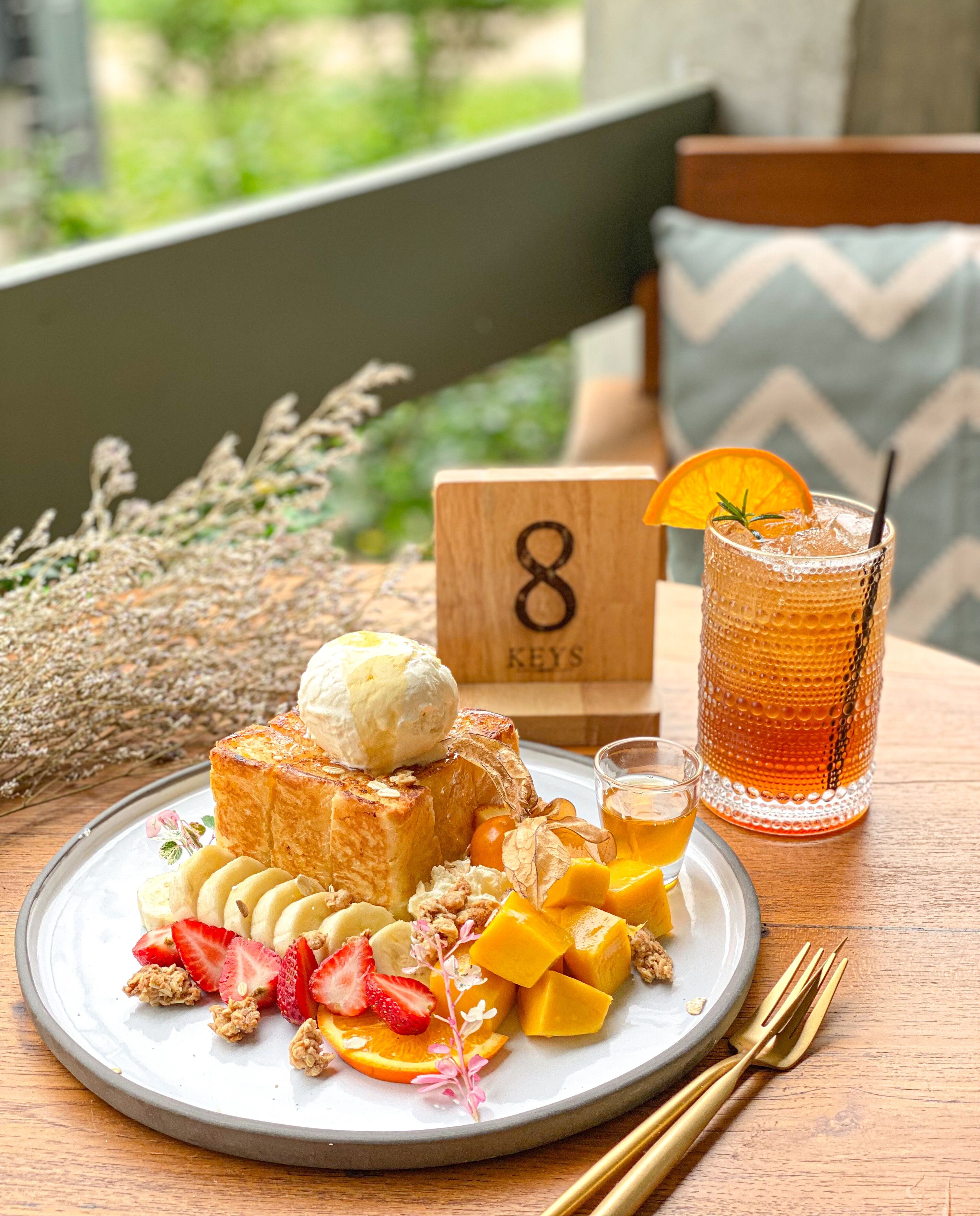 Desayuno con tostadas, fruta, helado y una bebida en un plato, junto a un cartel de madera con un número y una taza de té.
