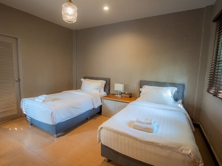 A hotel room with two single beds, a bedside table with a lamp, and a window with blinds.