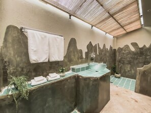 Un baño con lavamanos de vidrio, toallas y una planta en maceta.