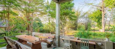 An outdoor patio with a wooden table and chairs, surrounded by a brick wall and greenery.