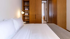 Quarto com cama grande, guarda-roupa de madeira e luminária suspensa.