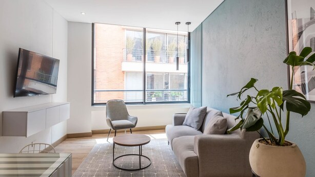 Uma sala de estar moderna com sofá, poltrona, TV e planta em vaso.