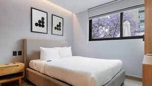 A modern bedroom with a large bed, a bedside table, and a window with a view of trees. - w* | Polished Loft in Polanco (Ciudad de México)