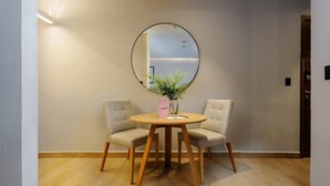 A room with a round wooden table, two beige chairs, a round mirror on the wall, and a small potted plant on the table. - w* | Polished Loft in Polanco (Ciudad de México)