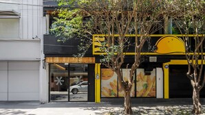 A building with a large glass window, a tree in front, and a yellow and black sign. - w* | Polished Loft in Polanco (Ciudad de México)