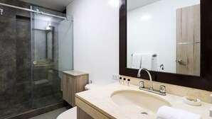 A modern bathroom with a glass-enclosed shower, a beige sink with a large mirror, and wooden cabinetry. - w * | Elegant 1BR in San Isidro (San Isidro)