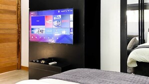 A modern bedroom with a large flat-screen TV mounted on a black wall, a wooden door, and a bed with a gray blanket. - LEADWORT HOTELS (Port Harcourt)