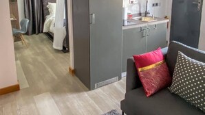 A compact living space with a kitchenette, a sofa with decorative pillows, and a bed with a canopy.