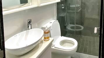 A modern bathroom with a large white sink, a toilet, and a glass-enclosed shower area.
