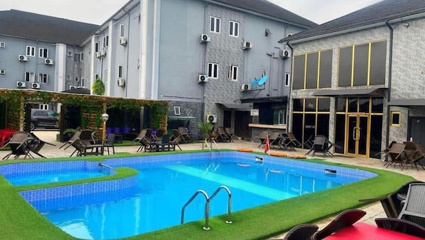 A swimming pool with lounge chairs and a building with multiple windows and air conditioning units.